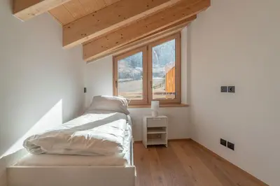 a small bedroom with a bed and two windows at Duplex Cermis in Cavalese