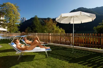 two women sitting on a lawn chair under an umbrella at Hotel Grones in Ortisei