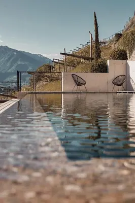 a pool of water with chairs and umbrellas at Weingut Pratenberg in Merano
