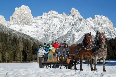 a group of people riding on a horse drawn sleigh in the mountains at Camping Castelpietra in Fiera di Primiero