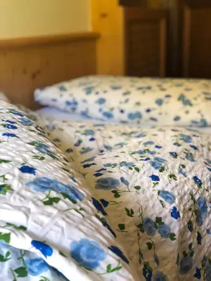 a bed with blue and white sheets with blue flowers at Garni al Barance in Selva di Cadore