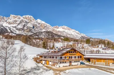 a large building with snow covered mountains in the background at Chalet Mortisa, Cortina design apartment in Col