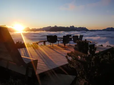 a table and chairs on a deck with a view of clouds at Berghotel zum Zirm in Collalbo