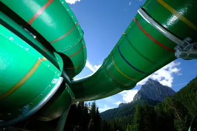 a green water slide with a mountain in the background at Vidor Resort in Pozza di Fassa