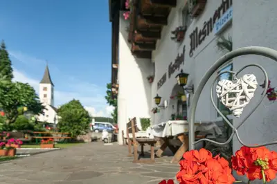 a bench with red flowers in front of a building at Gasthof Mesnerwirt in Auna di Sopra