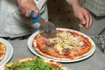 a person cutting a pizza with a pizza cutter at Gasthof Mesnerwirt in Auna di Sopra