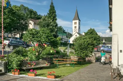a woman riding a bike past a garden with a church at Gasthof Mesnerwirt in Auna di Sopra