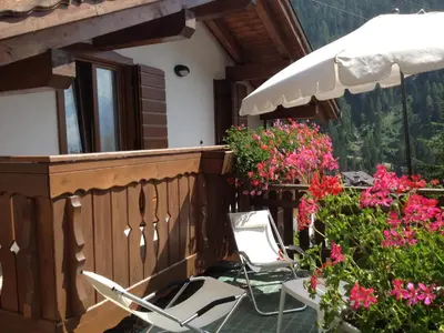a pair of chairs and an umbrella on a balcony with flowers at Casa Vacanze Villa Elena in Alleghe