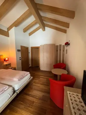 a bedroom with two beds and a red chair at Hotel Primula in Campitello di Fassa