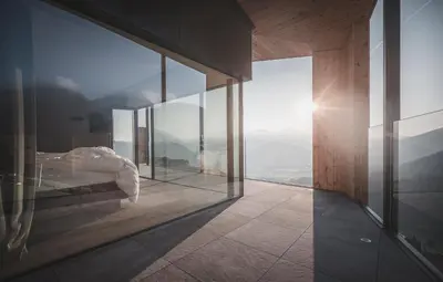 a bedroom with a view of the mountains through glass at Kronplatz-Resort Berghotel Zirm in Valdaora