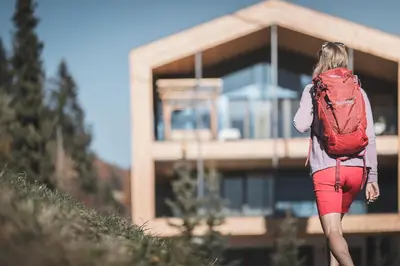 a woman with a red backpack walking in front of a building at Kronplatz-Resort Berghotel Zirm in Valdaora