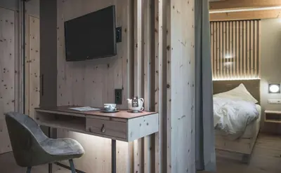 a desk with a chair and a tv on a bedroom at Kronplatz-Resort Berghotel Zirm in Valdaora