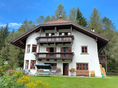 a large white house with a balcony and trees at Im weißen Schlössl Friedemann in Rasùn di Sotto
