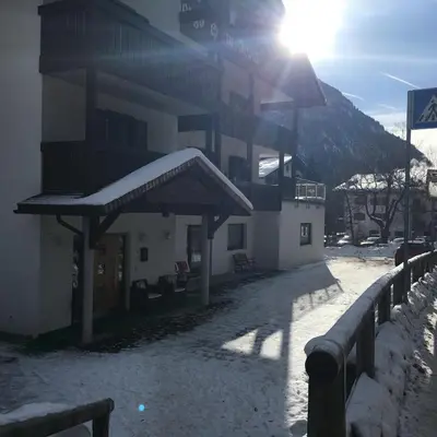 a snow covered building with the sun behind it at Garni Festil in Campitello di Fassa