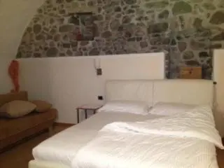 a white bed in a room with a stone wall at Tirso Apartament in Castello di Fiemme
