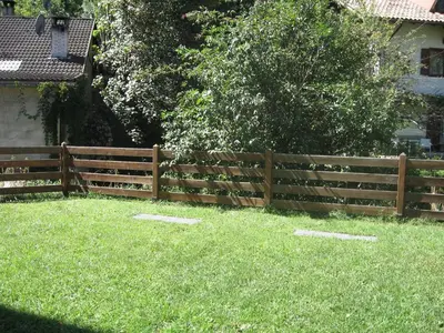 a wooden fence in a yard with green grass at Casa Franca in Cavalese