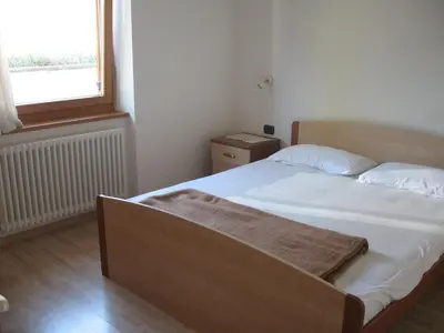 a small bedroom with a bed with white sheets and a window at Casa Franca in Cavalese