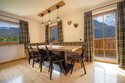 a dining room with a table and chairs and large windows at Schoenau Bio & SPA Family Apartments in San Pietro in Gardena