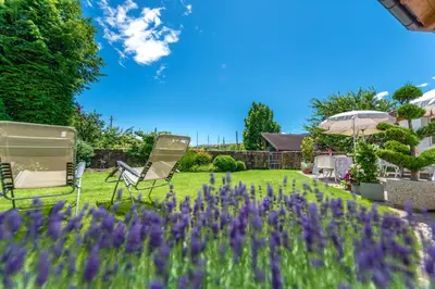 a garden with two chairs and an umbrella and purple flowers at Haus Oberhofer in Cornaiano