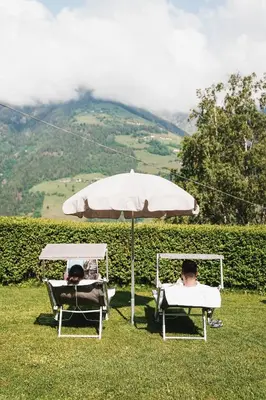 two people laying in lawn chairs under an umbrella at Hotel Mitlechnerhof in Schenna