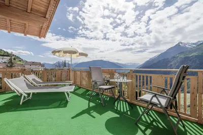 a deck with chairs and a table and an umbrella at Hotel Mitlechnerhof in Schenna