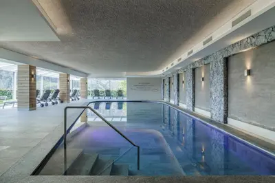 a swimming pool in a hotel lobby with chairs at Hotel Mitlechnerhof in Schenna
