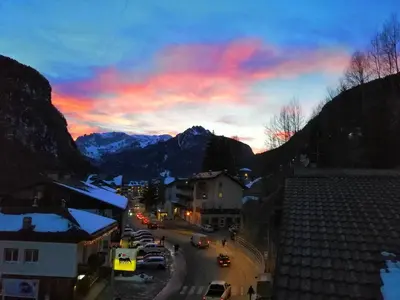 a town with cars parked on a street at sunset at San Cristoforo in Canazei