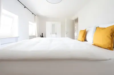 a white bedroom with a large white bed with yellow pillows at Huberhof Meran in Merano