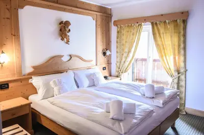 a bedroom with a large white bed with a window at Hotel Relais Grünwald in Cavalese