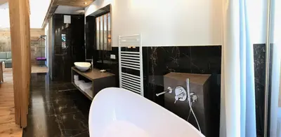 a bathroom with a white tub and a black wall at Hotel Enzian in Villa Ottone