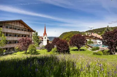 a village with a church and a field of flowers at Artnatur Dolomites Hotel & Spa in Siusi
