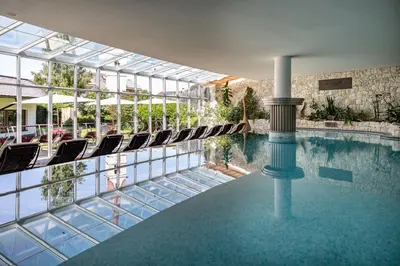 a swimming pool in a building with lounge chairs at Artnatur Dolomites Hotel & Spa in Siusi