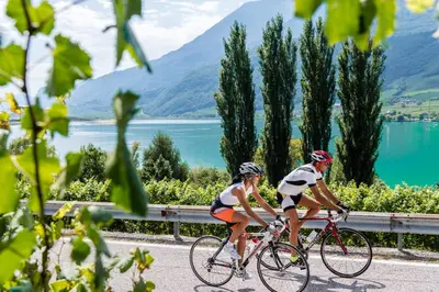 two people riding bikes on a road next to a lake at Hotel Torgglhof in Caldaro