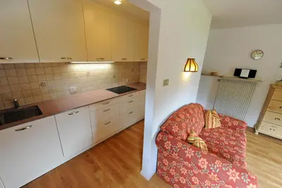 a living room with a red chair and a kitchen at Apartments Villa Rosa in Selva di Val Gardena
