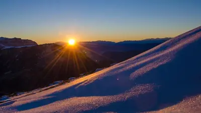 a snow covered hill with the sun in the background at Hotel Garni Ruscel in Santa Cristina in Val Gardena