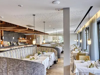 a restaurant with white tables and chairs and windows at Hotel Traubenheim in Tirolo