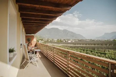 a woman sitting at a table on a balcony looking at a vineyard at Hotel Elisabeth in Merano