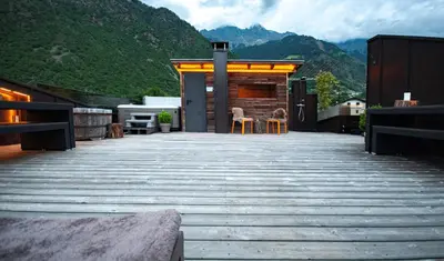 a wooden deck with a building with mountains in the background at Alpenchalet Apartments in Parcines