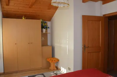 a bedroom with a bed and a cabinet and a chair at Appartamenti Vincenzo E Marcella in Campitello di Fassa