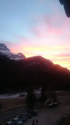 a sunset over a mountain with cars parked in a parking lot at Rododendro Apartment in Passo San Pellegrino