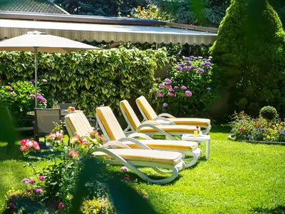 a row of lawn chairs and an umbrella in a yard at Pension Lahn in Rablà