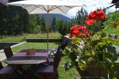 a table and chairs with an umbrella and red flowers at Chalet Do Costa in Pozza di Fassa