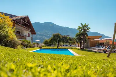 a resort with a swimming pool and mountains in the background at Hotel und Residence Johanneshof in Cermes