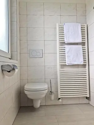 a bathroom with a toilet and towels on a shelf at Pension Planta in Merano