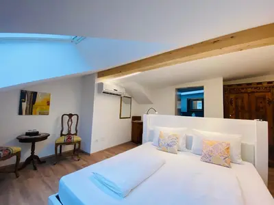 a bedroom with a large white bed and a chair at Hotel Garni Vinea Montis in Termeno