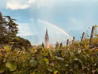 a rainbow over a garden with a clock tower at Hotel Garni Vinea Montis in Termeno