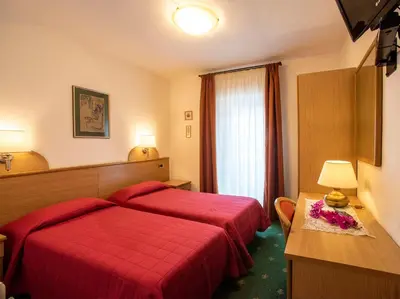 a hotel room with a red bed and a window at Hotel Adriana in Alleghe