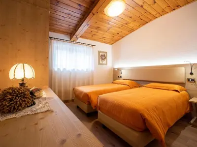two beds in a bedroom with wooden ceilings and wood floors at Hotel Adriana in Alleghe