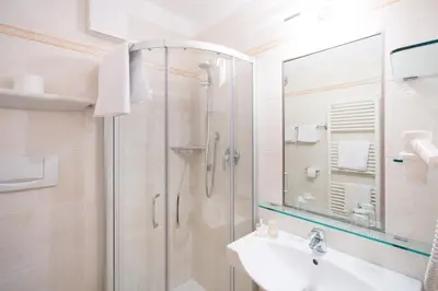 a white bathroom with a shower and a sink at Garni Pluner in Schenna