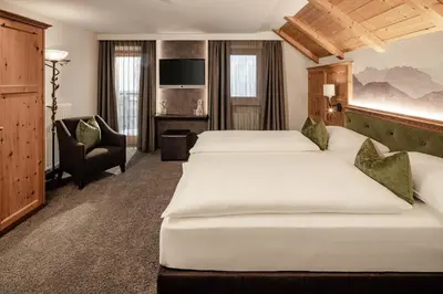 a hotel room with two beds and a chair at Boutique & Fashion Hotel Maciaconi - Gardenahotels in Santa Cristina in Val Gardena
